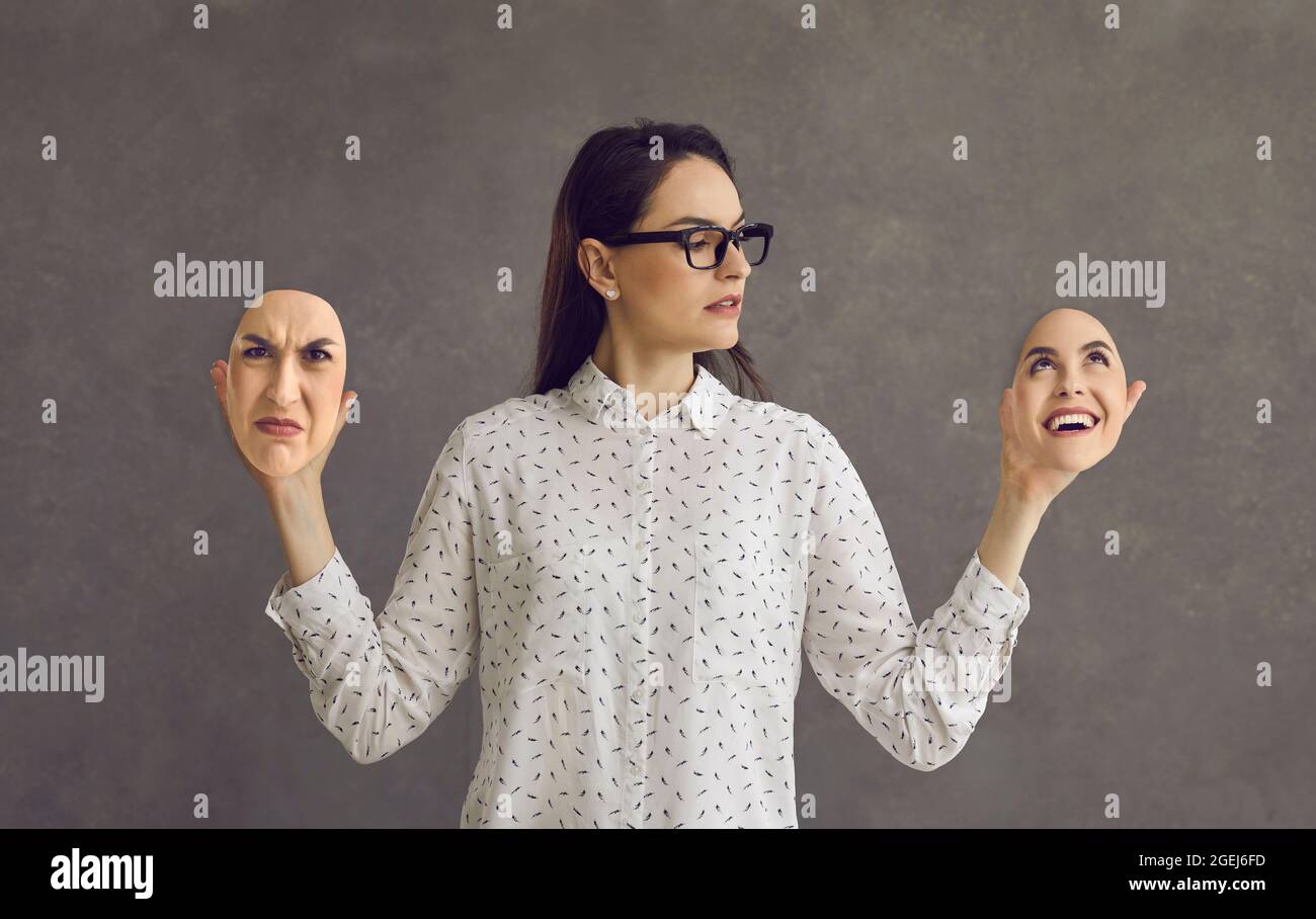 Junge Frau mit bipolarer Störung, die zwei Gesichtsmasken mit entgegengesetzten Emotionen hält Stockfoto