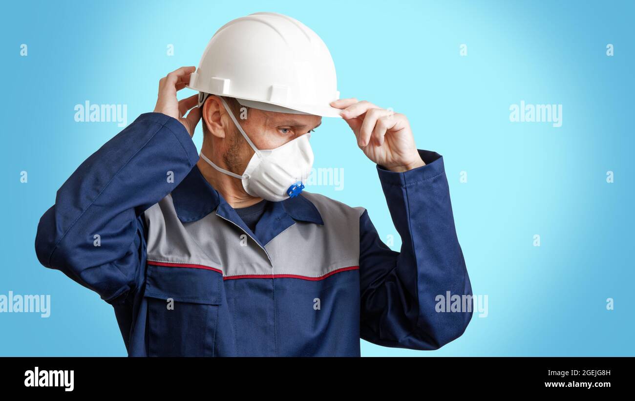 Porträt eines Mannes in einem weißen Konstruktionshelm, Atemschutzmaske und  Arbeitskleidung, isoliert auf blau. Copyspace Stockfotografie - Alamy