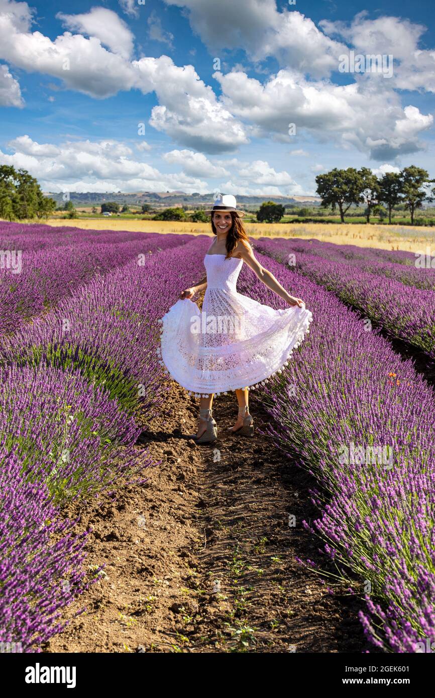 Glückliche junge Frau, die mit ihrem weißen Kleid inmitten eines blühenden Lavendelfeldes spielt. Konzept von Wohlbefinden und Glück. Stockfoto