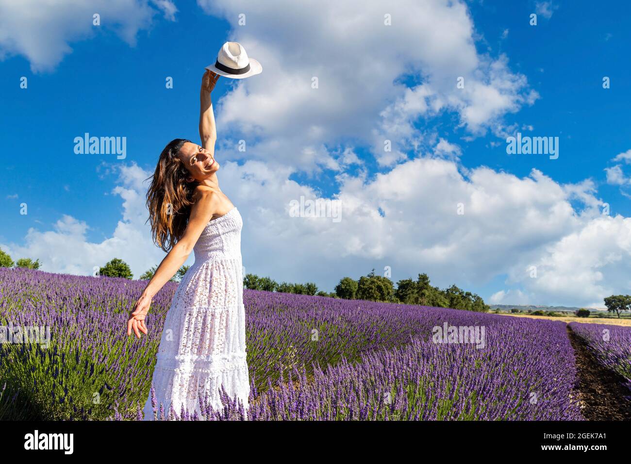 Junge glückliche Frau tanzt in einem Lavendelfeld und hebt ihren Hut an den blauen Himmel. Konzept des Wohlbefindens in der Natur und Freiheit. Stockfoto