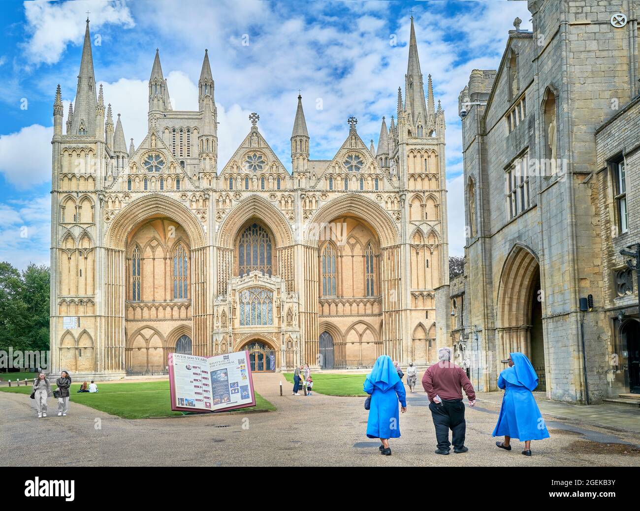 Ein englischer Priester und zwei afrikanische Nonnen gehen in Richtung der Westwand der mittelalterlichen christlichen Kathedrale in Peterborough, England, aus dem 13. Jahrhundert. Stockfoto