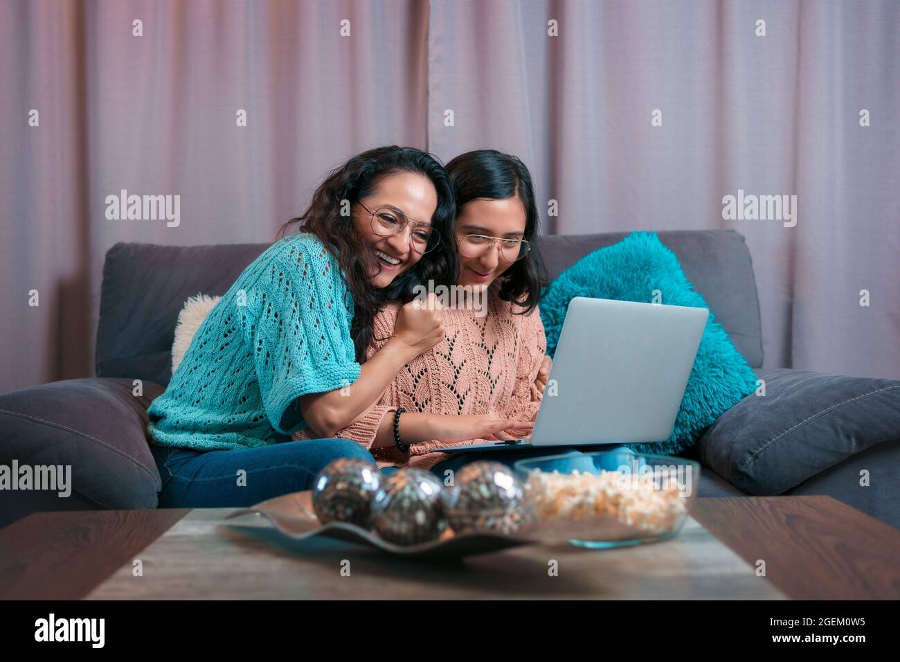 Horizontale Ansicht einer Mutter und ihrer Tochter mit einem Laptop, die Tochter zeigt ihr etwas auf dem Computer und die Mutter umarmt ihre Tochter in Appreci Stockfoto