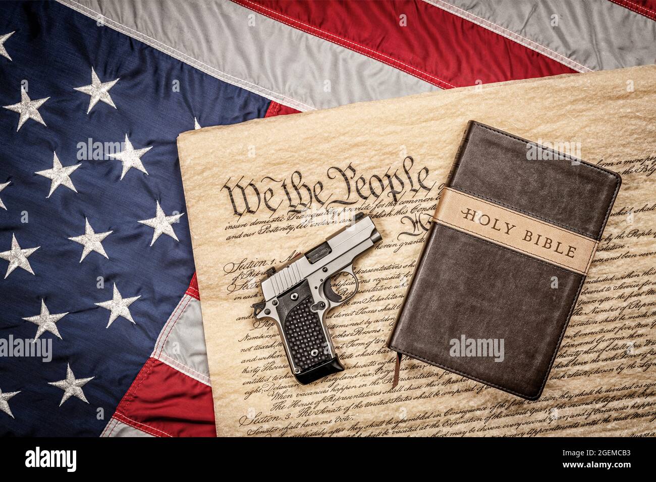 Eine heilige bibel und eine Handfeuerwaffe stehen auf der Verfassung der Vereinigten Staaten und der amerikanischen Flagge, die ein Sinnbild für Religionsfreiheit ohne Verfolgung ist. Stockfoto