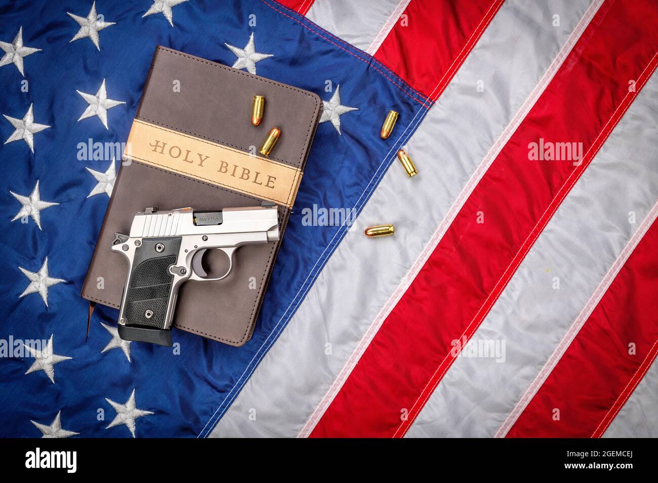 Eine Waffe und eine heilige bibel stehen auf einer amerikanischen Flagge, die Gott, Waffen und Religionsfreiheit repräsentiert. Stockfoto