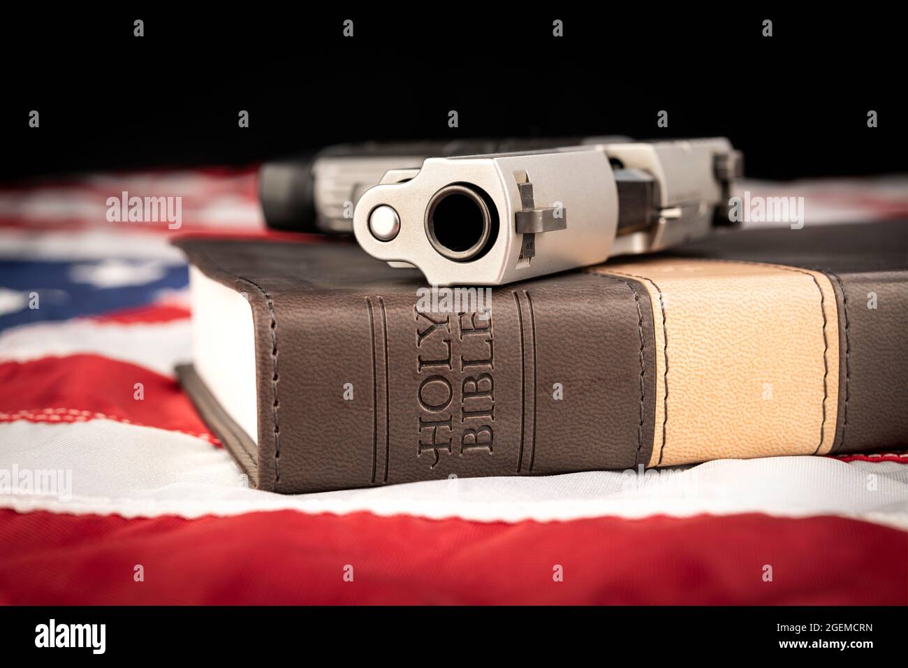 Eine Waffe und eine heilige bibel stehen auf einer amerikanischen Flagge, die Gott, Waffen und Religionsfreiheit repräsentiert. Stockfoto