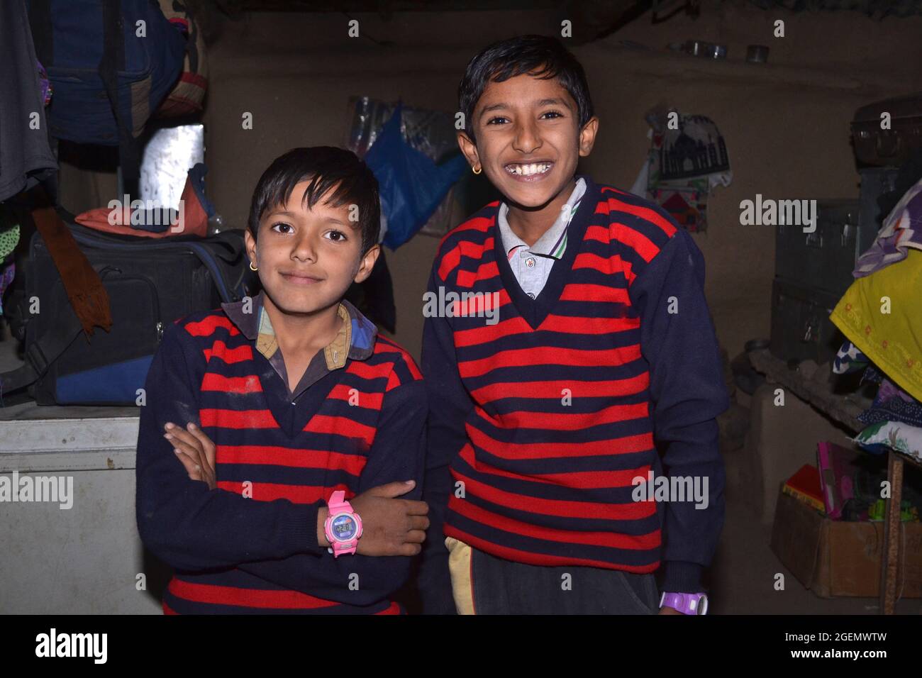 Zwei indische ländliche Kinder, die in ihren Häusern auf die Kamera schauen, tragen blaue Pullover mit roten Streifen. Kalte Nächte des indischen Dorfes. Stockfoto