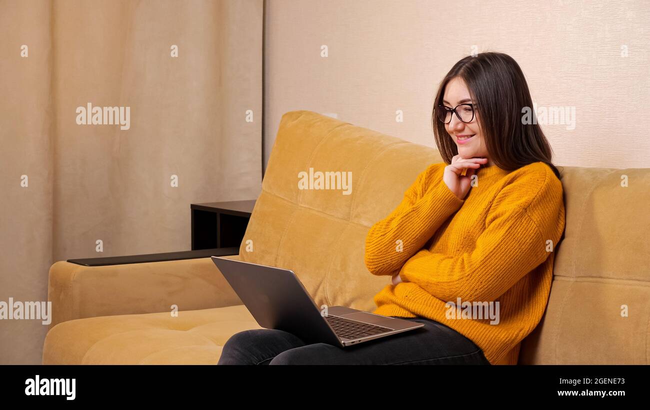 Seriöse junge Frau mit langen lockeren Haaren sitzt am Laptop Stockfoto