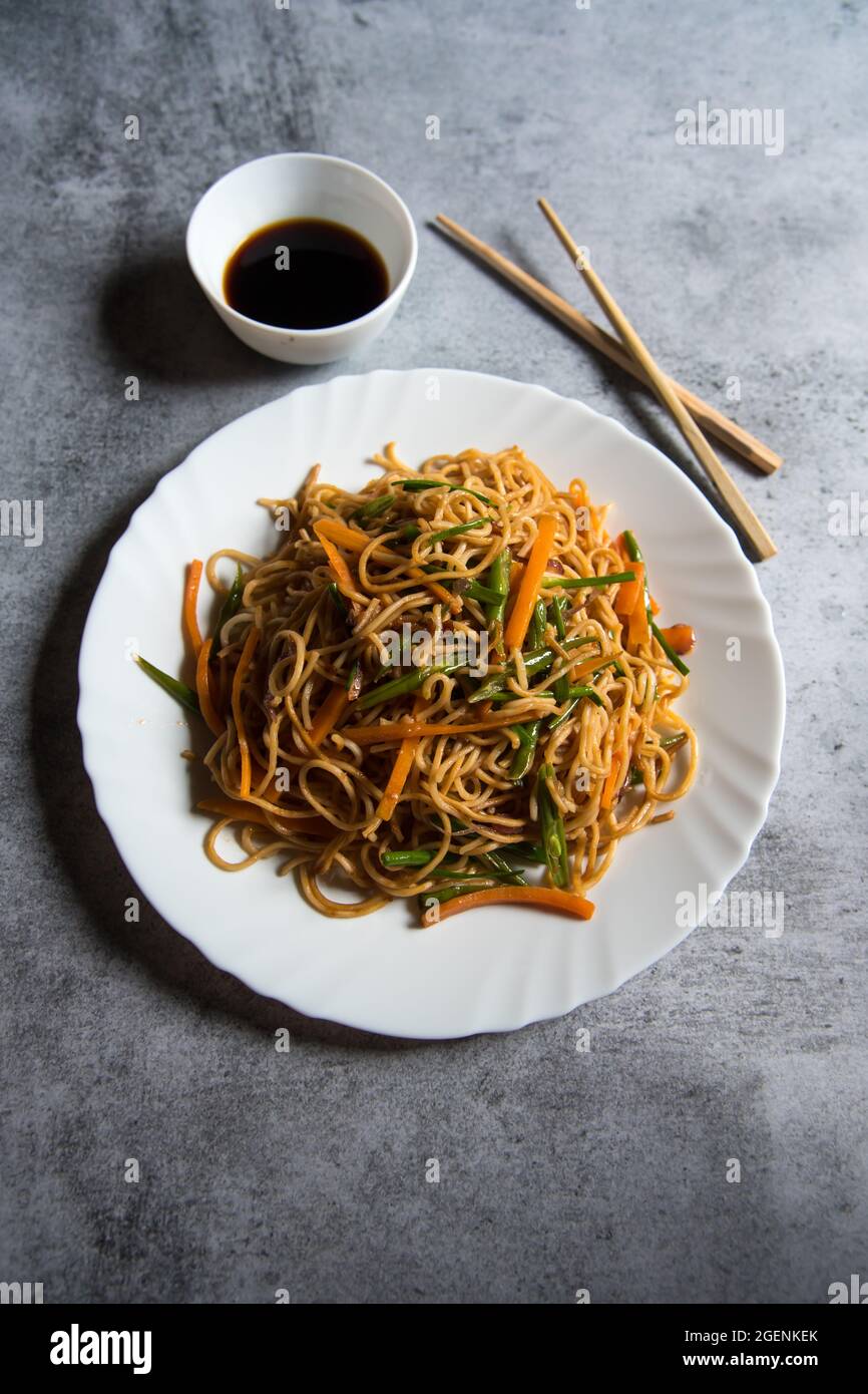 Schezwan-Nudeln, die mit gehacktem Gemüse, Fleisch und udon-Nudeln auf einem weißen Teller zubereitet werden. Stockfoto