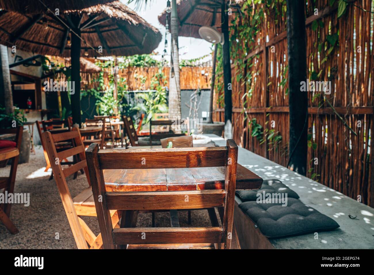 Leere Holzstühle und -Tische mit Strohschirm im Café im Freien Stockfoto