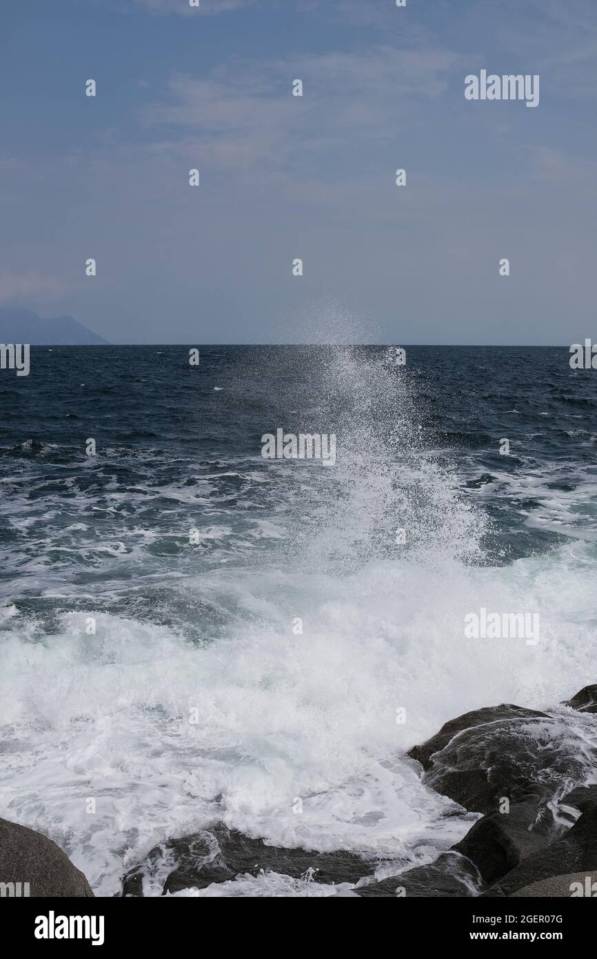 Eine Welle, die gegen einen Felsen stürzt und in Chalkidiki Griechenland einen großen Spritzer in der Luft erzeugt Stockfoto