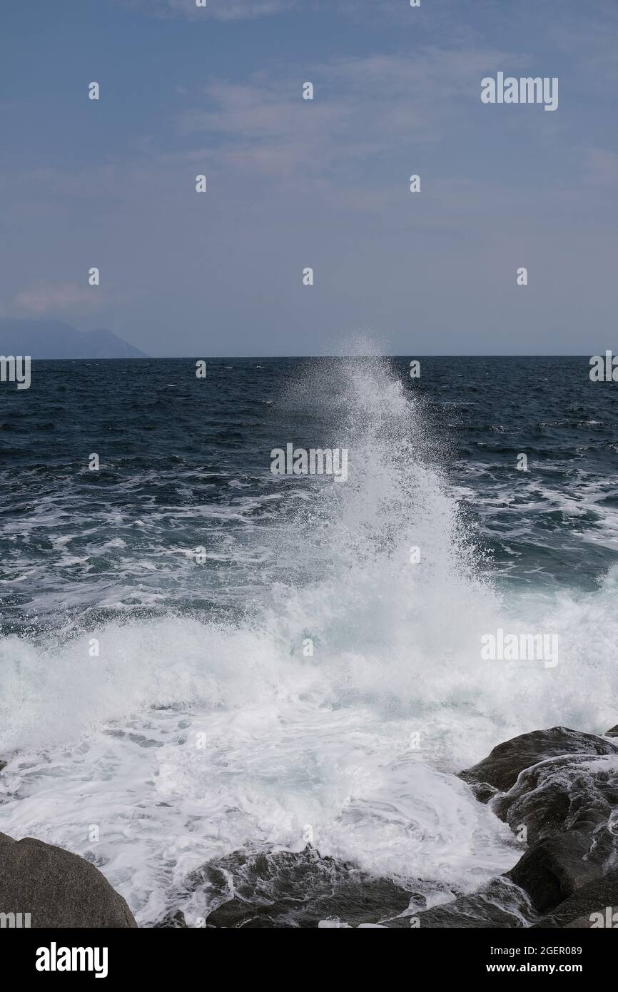Eine Welle, die gegen einen Felsen stürzt und in Chalkidiki Griechenland einen großen Spritzer in der Luft erzeugt Stockfoto