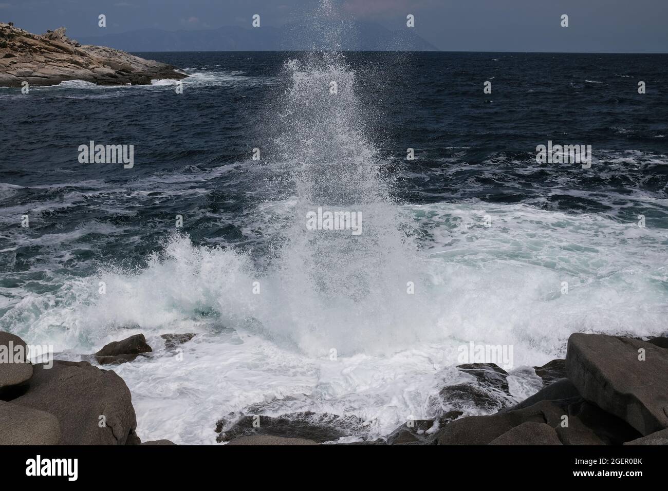 Eine Welle, die gegen einen Felsen stürzt und in Chalkidiki Griechenland einen großen Spritzer in der Luft erzeugt Stockfoto