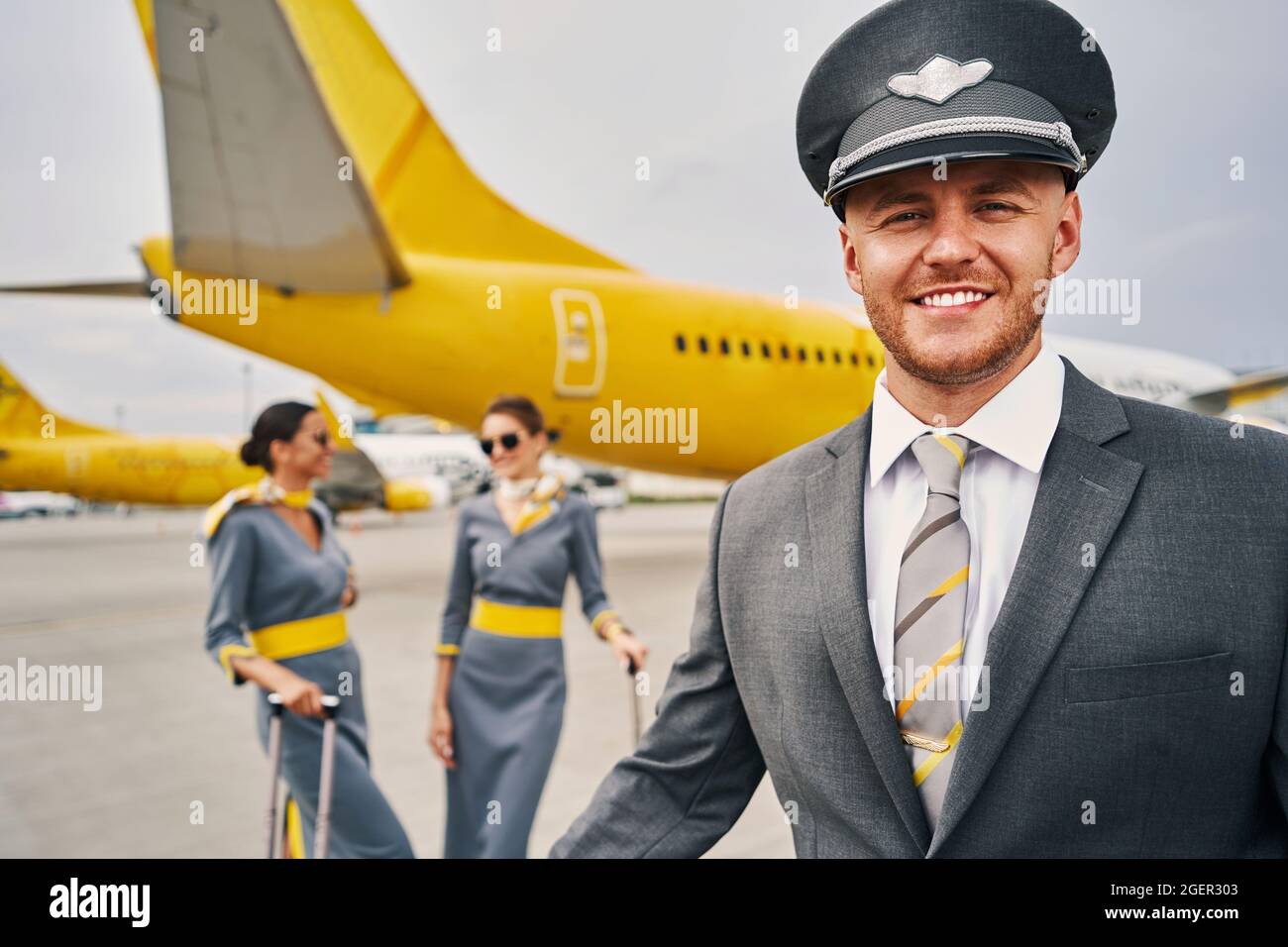 Lächelnder Flieger und seine weiblichen Kollegen auf dem Flugplatz Stockfoto