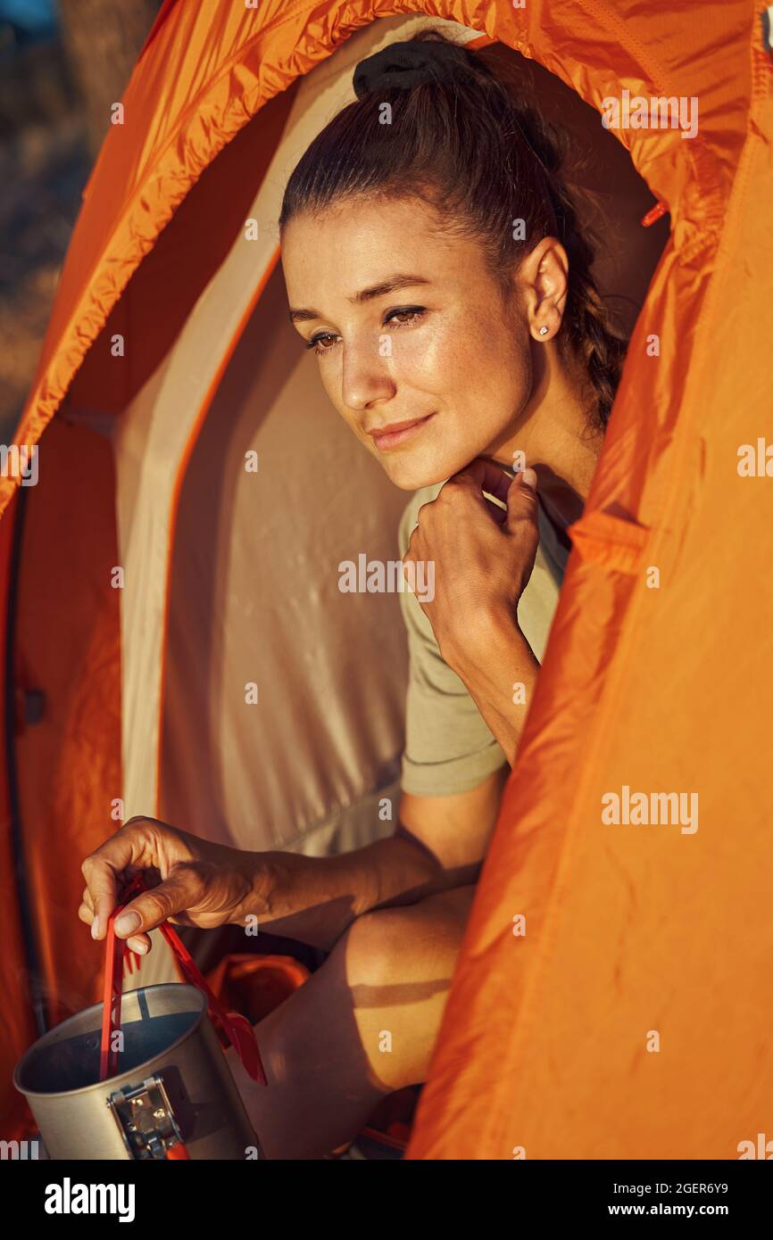 Frau bewundert den Sonnenuntergang, während sie im Zelt Tee kocht Stockfoto Frau bewundert den Sonnenuntergang, während sie im Zelt Tee kocht Stockfoto