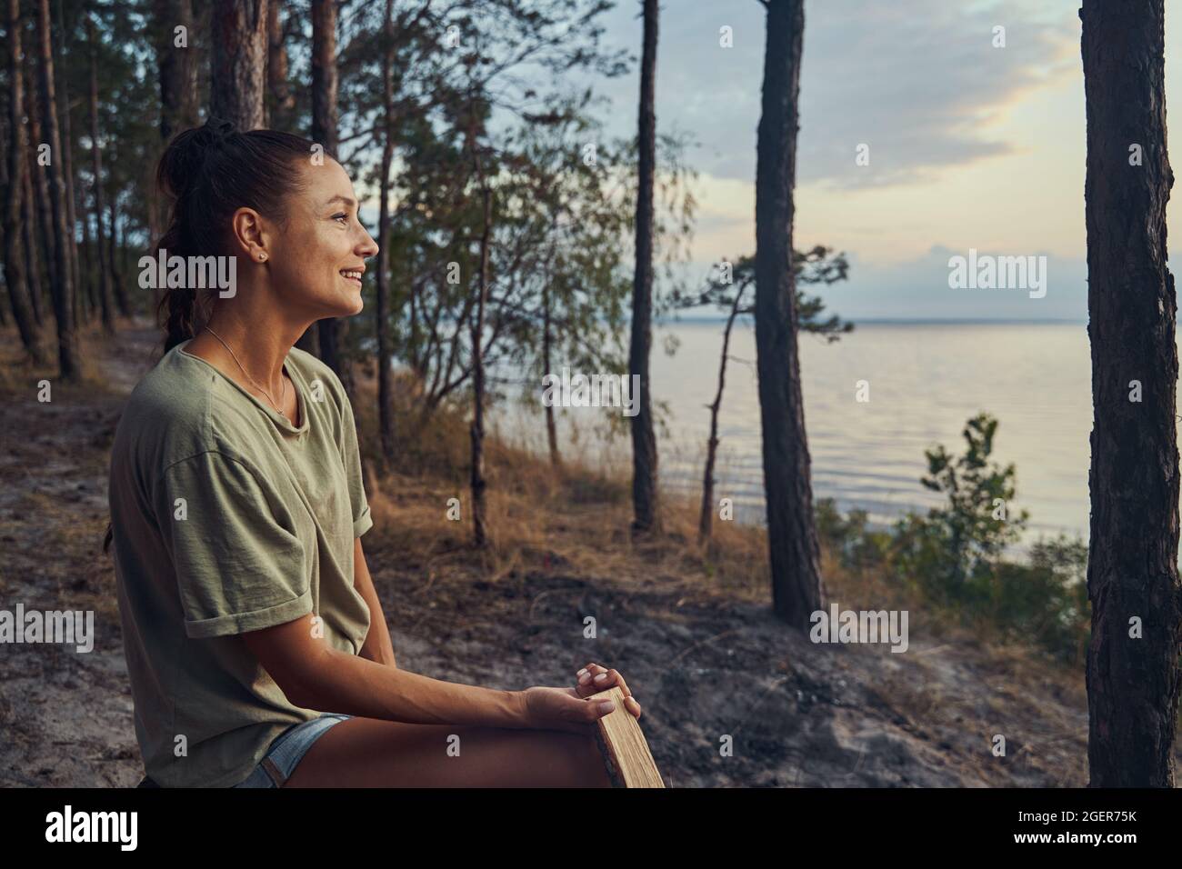 Frau, die einen Blick auf den See genießt, während sie einen Baumstamm hält Stockfoto Frau, die einen Blick auf den See genießt, während sie einen Baumstamm hält Stockfoto