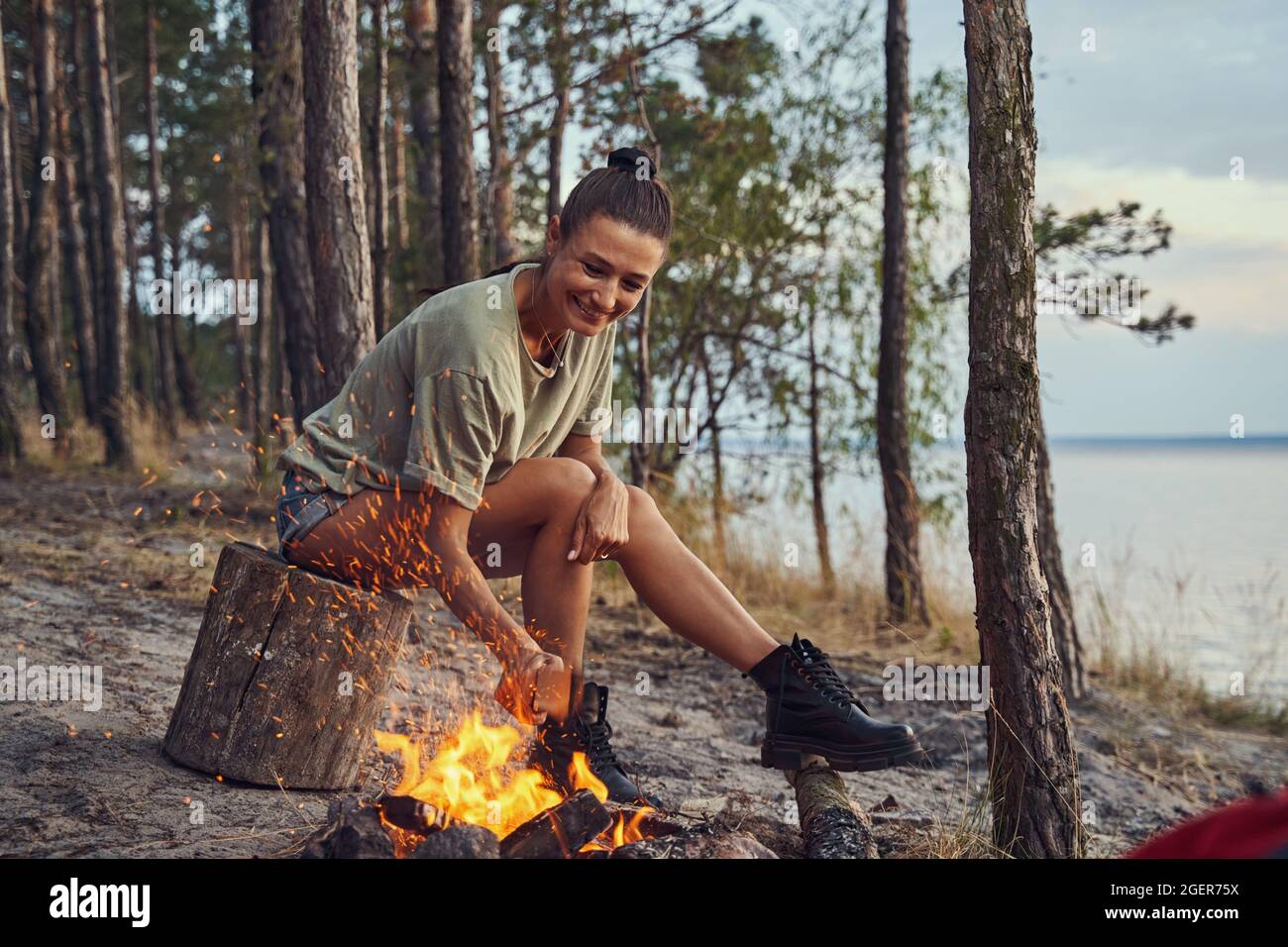 Glücklicher Camper wirft ein Log auf das Feuer Stockfoto Glücklicher Camper wirft ein Log auf das Feuer Stockfoto