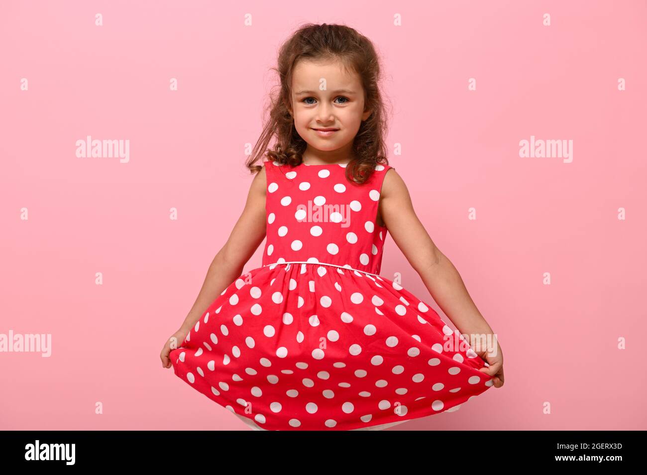Portrait von niedlichen charmanten Mädchen in einem rosa Kleid mit weißen  Punkten posiert auf rosa Hintergrund niedlich lächelnd und hält den Boden  des Kleides mit ihm Stockfotografie - Alamy