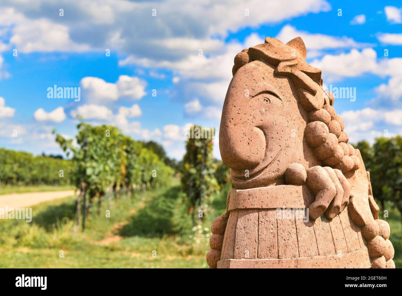 Wiesloch, Deutschland - August 2021: Lustige Skulptur des weingottes namens 'Speedy Bacchus' mit verschwommenem Weinberg im Hintergrund Stockfoto