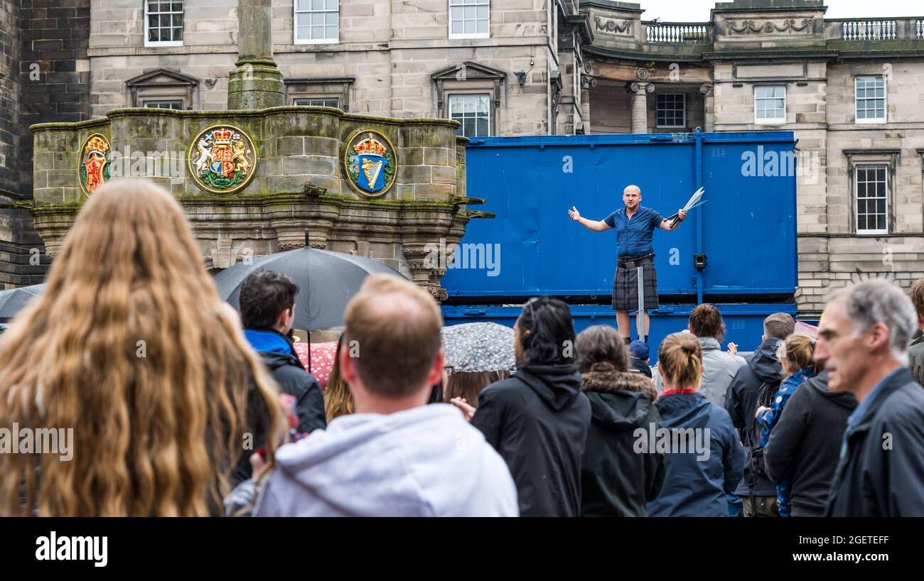 Royal Mile, Edinburgh, Schottland, Großbritannien, 21. August 2021. UK Wetter: Regen am Edinburgh Festival Fringe. Das trostlos nasse Wetter schreckt die Fringe-Massen oder die Straßenkünstler auf einem zurückgeschreckt Festival in diesem Sommer nicht ab. Ein Mann mit einem Kilt, der auf einer Leiter balanciert und mit Macheten jongliert Stockfoto