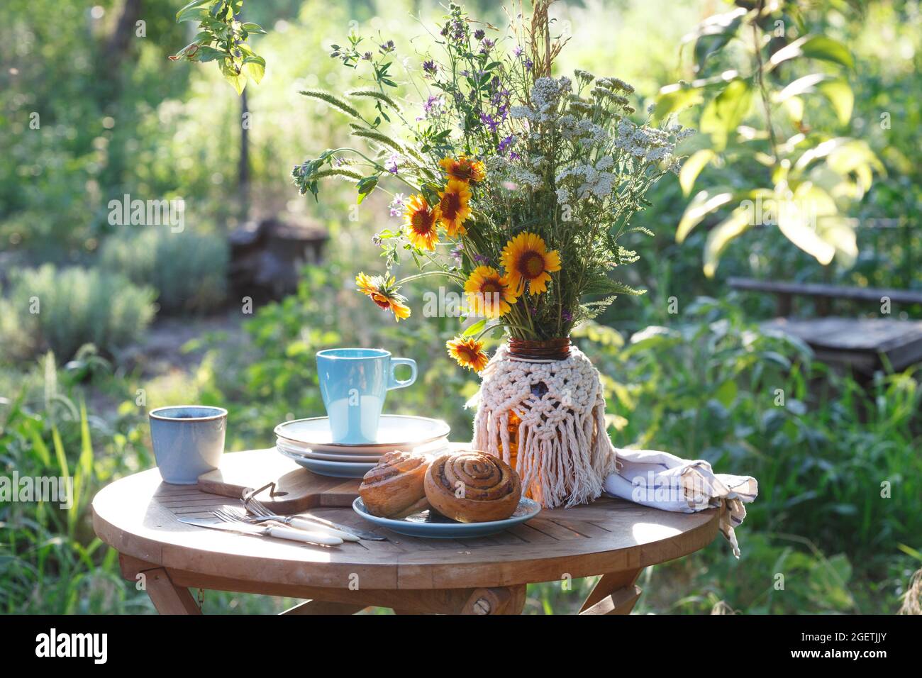 Garten- und Teeparty im Landhausstil. Stillleben - Zimtrollen, Tassen, Geschirr und eine Vase mit Wildblumen Stockfoto