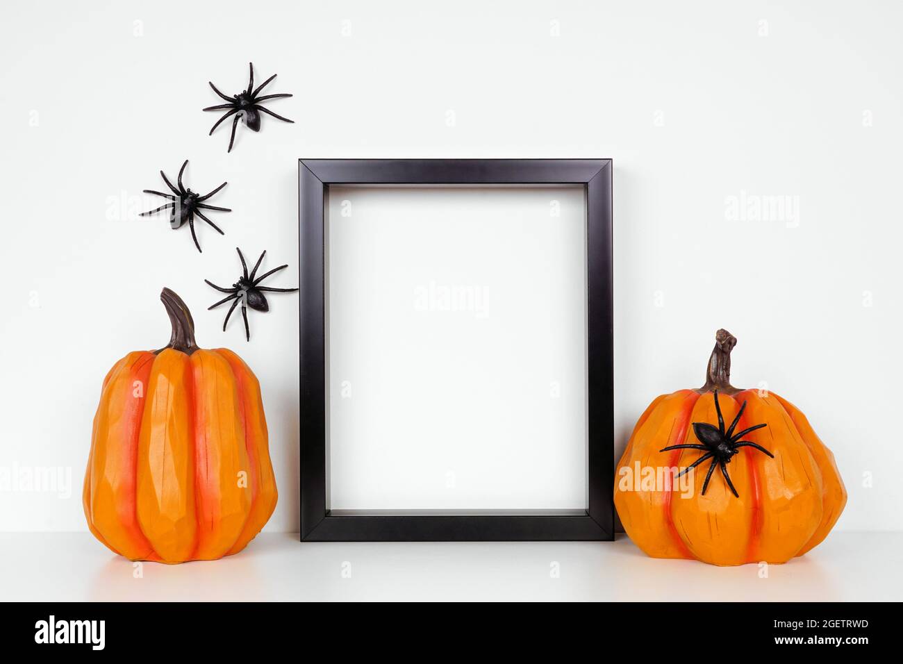 Schwarzer Rahmen mit Kürbis-Dekor auf einem Regal oder Schreibtisch. Halloween-Konzept. Porträtrahmen an einer weißen Wand mit Spinnen. Stockfoto