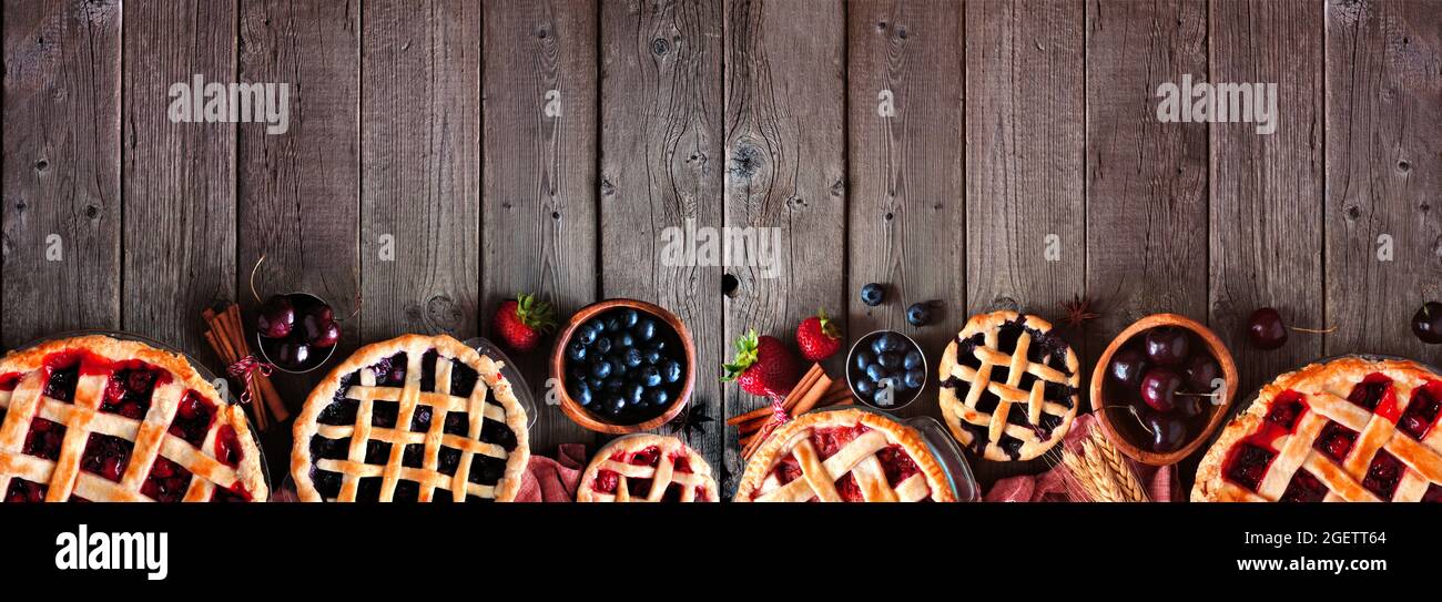 Auswahl an hausgemachten herbstlichen Obstkuchen. Draufsicht Rahmen über einem dunklen Holz Banner Hintergrund mit Kopierraum. Kirsche, Erdbeere und Heidelbeere. Stockfoto