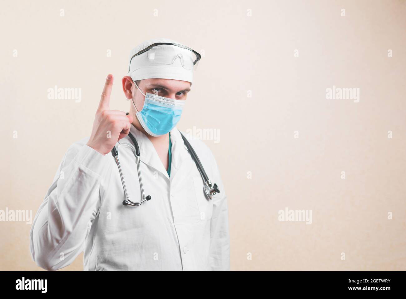 Junger Arzt in weißem Laborkittel, Schutzbrille und schützender Atemmaske, die auf den gelben Hintergrund zeigt. Stockfoto