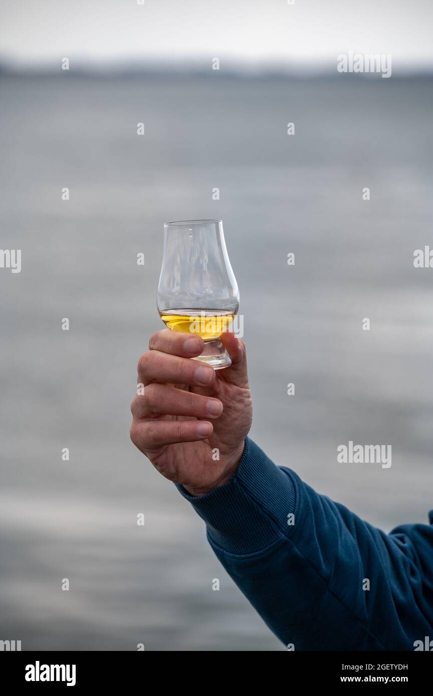 Hand hält einen Schluck Single Malt Scotch Whisky an der Küste In Schottland Stockfoto