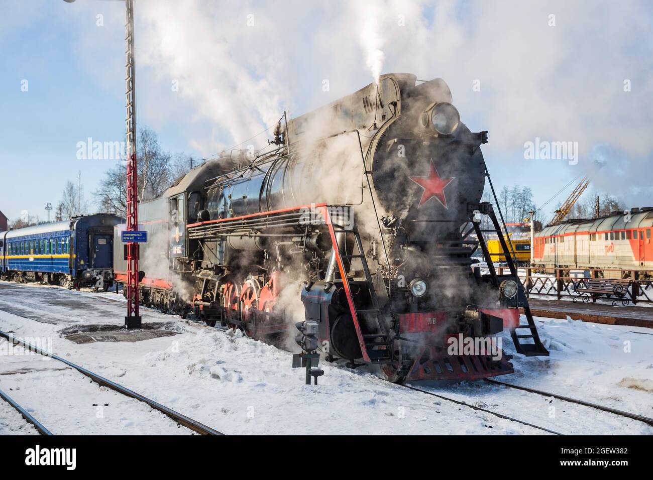 SORTAVALA, RUSSLAND - 10. MÄRZ 2021: Eine alte sowjetische Dampflokomotive klammert sich am Bahnhof von Sortavala an einen Personenzug Stockfoto