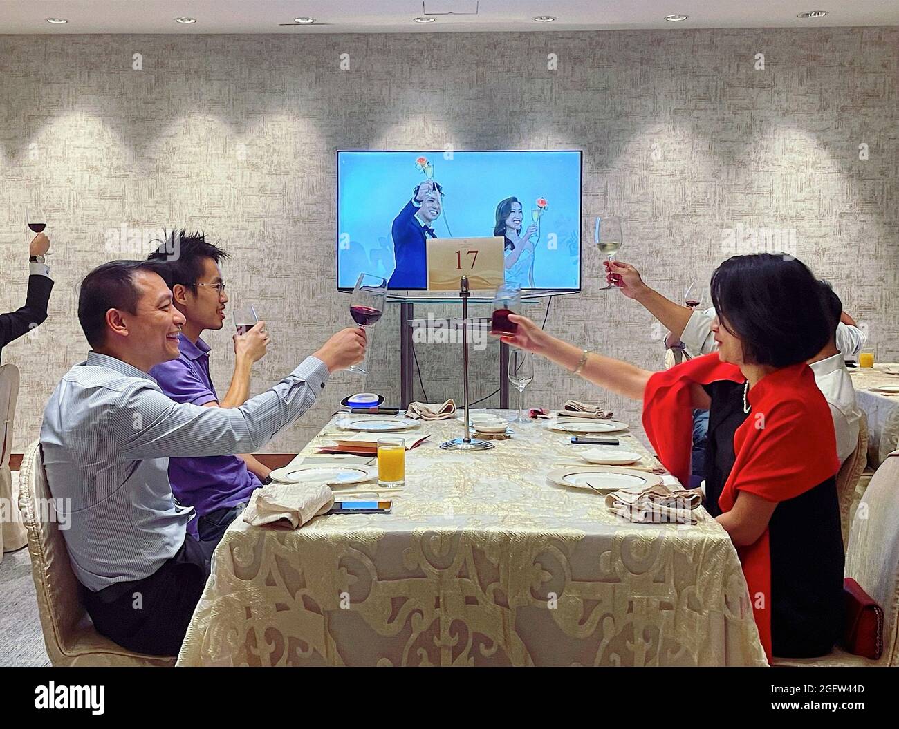 Hongkong, China. August 2021. Die Gäste werden nach der Hochzeit über einen Live-Bildschirm mit dem Brautpaar toasting gesehen.die sozialen Distanzierungsmaßnahmen in Hongkong haben die Art und Weise verändert, während einer Hochzeit zu feiern. Hochzeitszeremonien sind nur für bis zu 50 Teilnehmer erlaubt, wobei maximal 4 Personen an jedem Tisch Platz finden. Viele Paare entscheiden sich dafür, ihre Hochzeit online zu haben, um mehr Familien und Freunde einzubeziehen. Kredit: SOPA Images Limited/Alamy Live Nachrichten Stockfoto