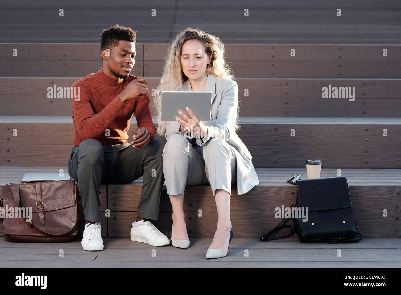 Zwei interkulturelle Büroangestellte, die bei einem Meeting Online-Daten auf dem Tablet-Bildschirm durchschauen Stockfoto