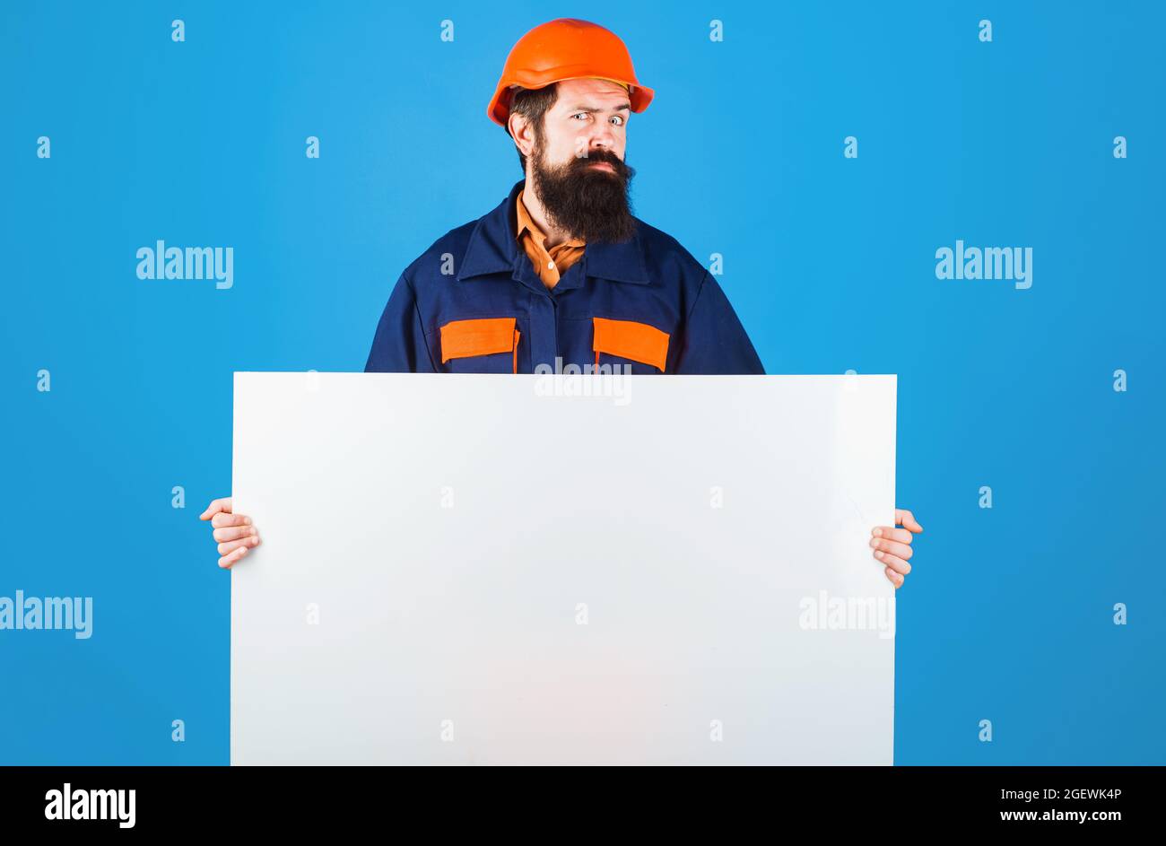 Seriöse Baumeister Mann in Schutzhelm und Kleidung mit Werbebanner. Bauarbeiter in Harthut zeigt ein leeres Schild. Stockfoto