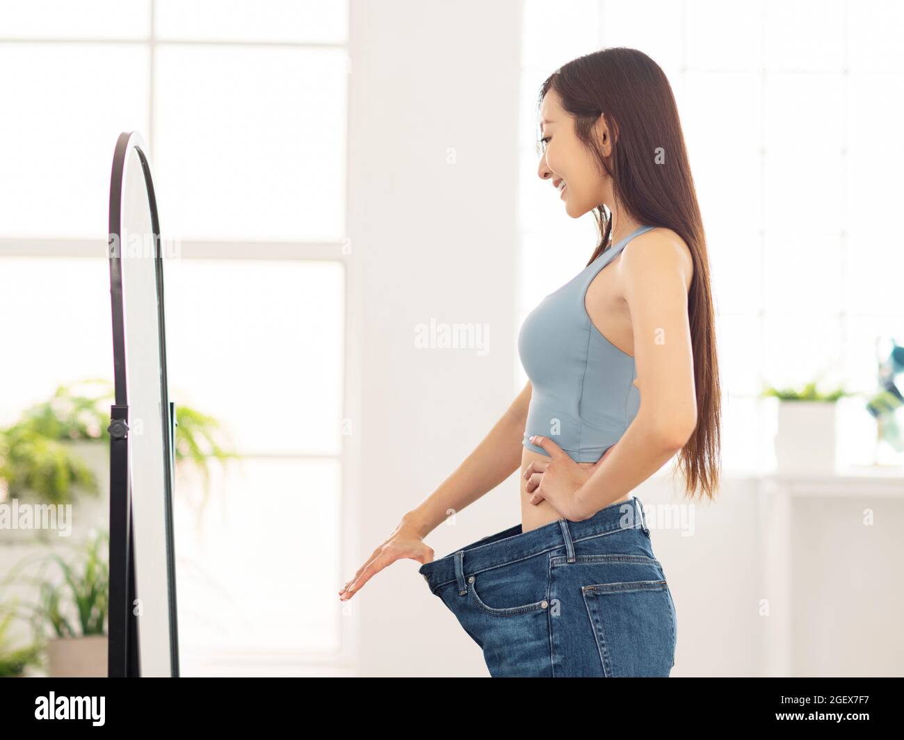 Junge Frau in Jeans groß stehend vor dem Spiegel.Gewichtsverlust. Stockfoto