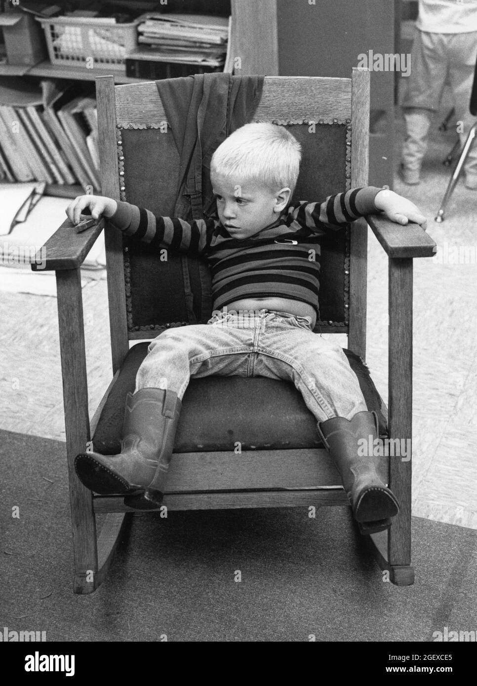 Austin Texas USA, um 1993: Pre-School-Junge in Cowboystiefeln, die im Kindertageszimmer eine Auszeit auf dem Stuhl machen. ©Bob Daemmrich Stockfoto