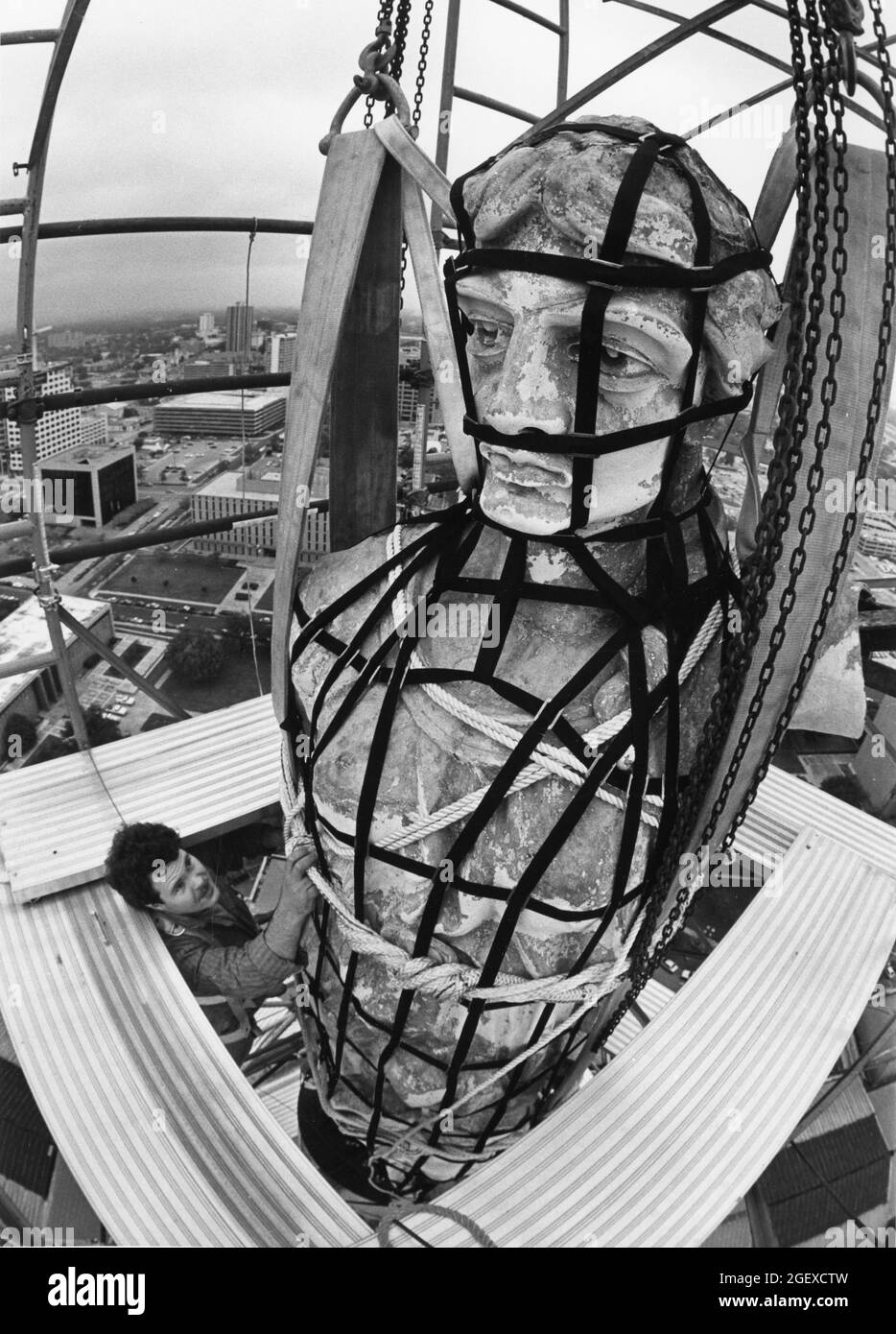 Austin, Texas, USA, um 1984: Arbeiter sichert sich ein Geschirr um die Statue der Göttin der Freiheit auf der Kuppel des Texas Capitol Gebäudes, bevor Besatzungen die Statue für Restaurierungsarbeiten entfernen. ©Bob Daemmrich Stockfoto