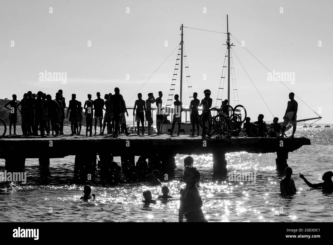 Salvador, Bahia, Brasilien - 09 2019. März: Silhouette junger Menschen, die beim gelben Sonnenuntergang am Strand von Ribeira in Salvador von der Crush-Brücke springen (B Stockfoto