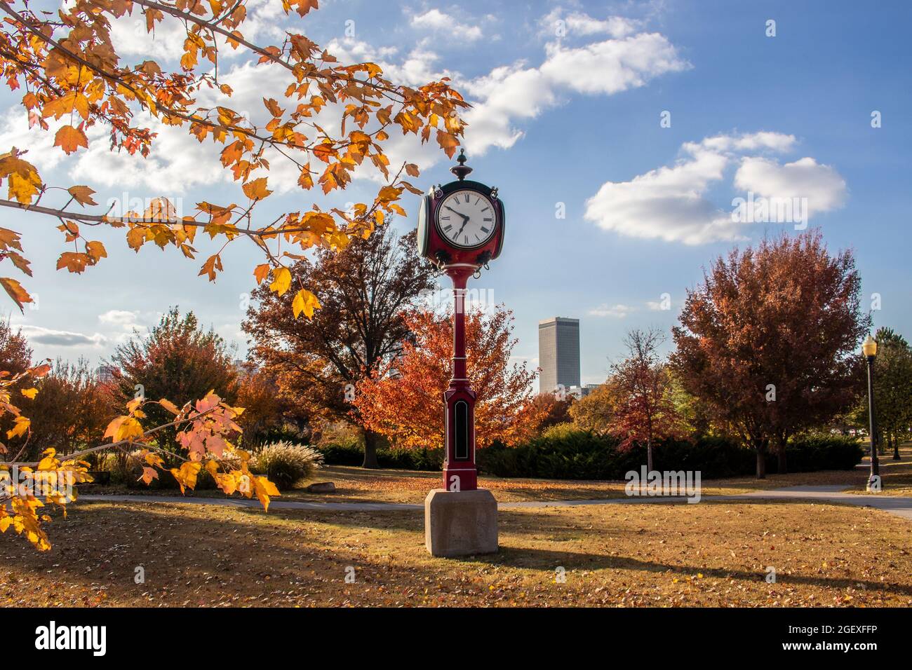 Vintage rote Standuhr im Herbstpark mit Wolkenkratzern der Stadt In der Ferne und bunte Blätter Rahmen - selektiver Fokus Stockfoto