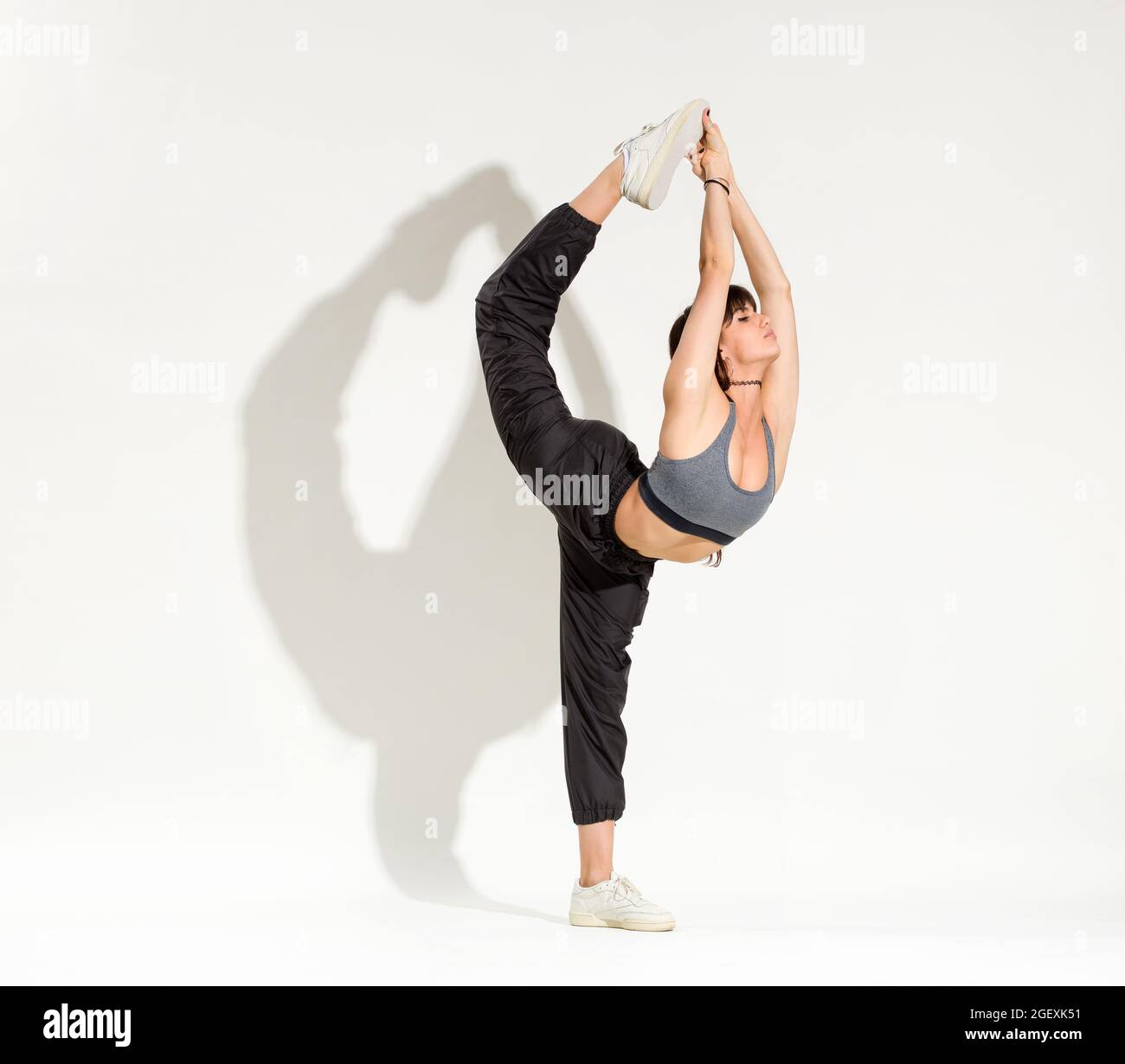 Fit athletische schöne junge Frau trägt ein Hip-Hop-Outfit tun eine Biellman Figur Skating Pose balanciert auf einem Bein, während sich bis sie zu berühren Stockfoto