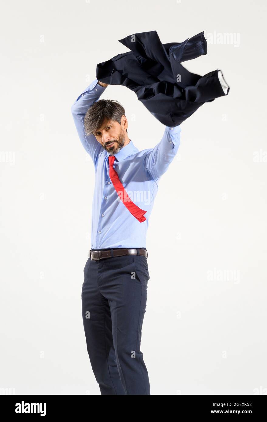 Stilvoller Geschäftsmann, der seine Jacke isoliert auf Weiß aufsetzt und sie über seinem Kopf schwingt, während er seine Arme in die Ärmel steckt Stockfoto