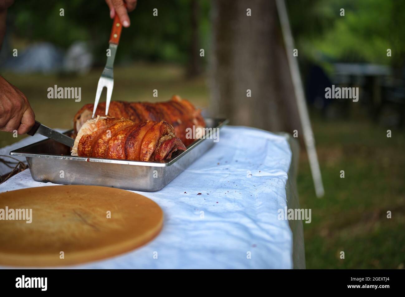 Zugeschnittenes Foto von Menschenhänden, die Schweinefleisch auf dem Spieß schneiden Stockfoto