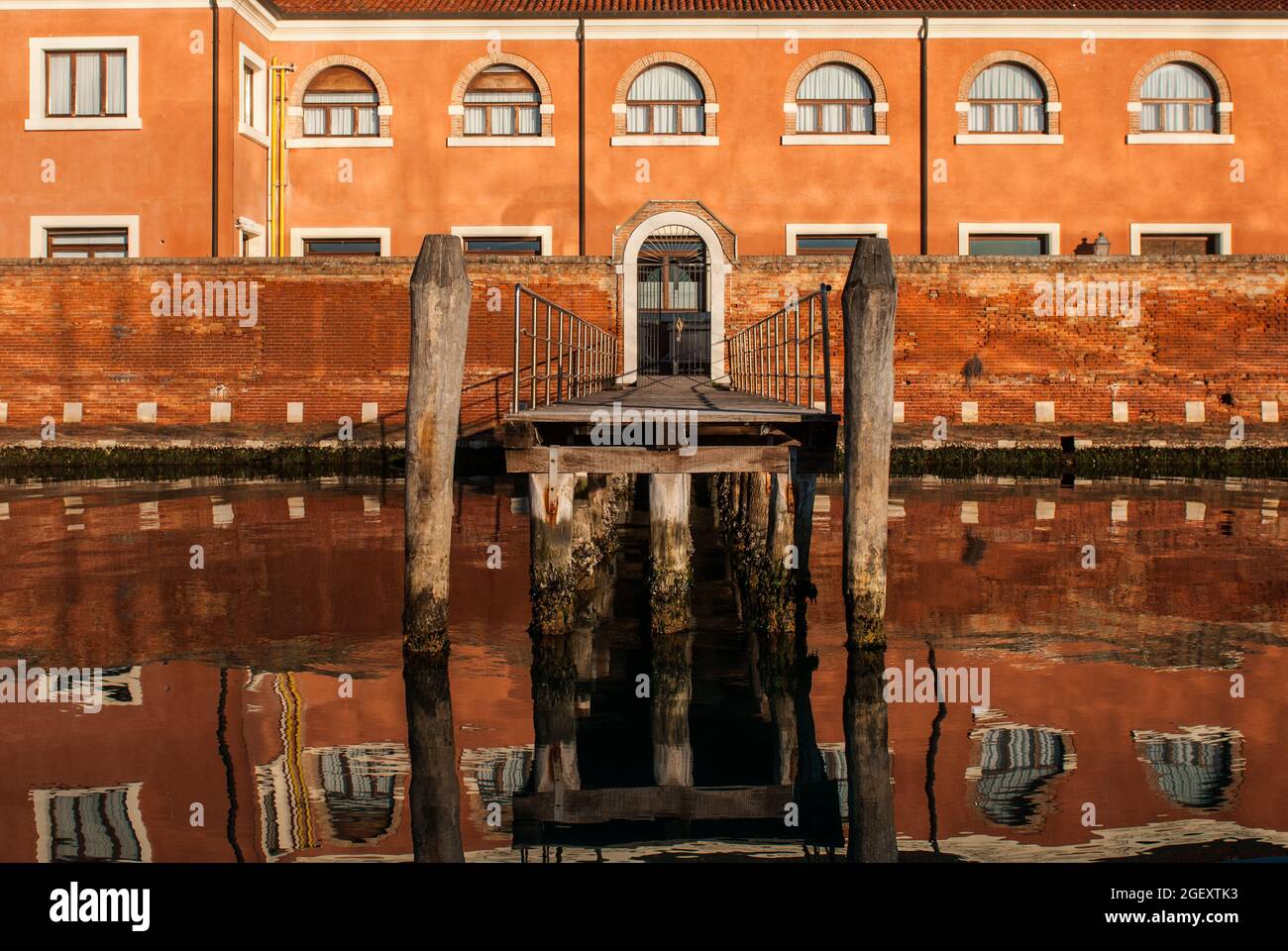 Ein Küstengebäude mit einer Brücke, die sich auf dem Wasser auf der Insel San Servolo in Venedig, Italien, widerspiegelt Stockfoto