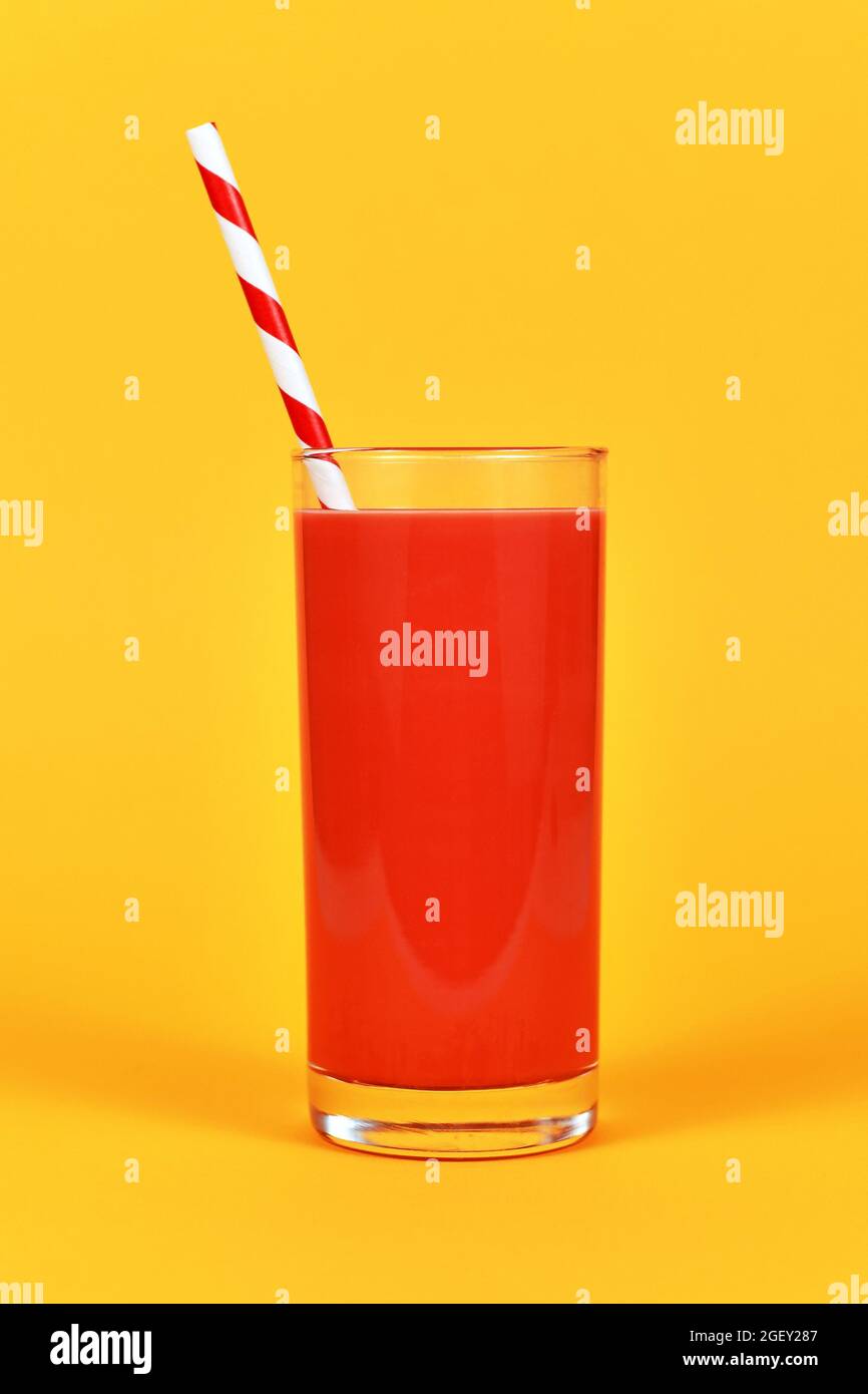 Volles Glas mit rotem Saft und gestreiftem Trinkhalm vor gelbem Hintergrund Stockfoto