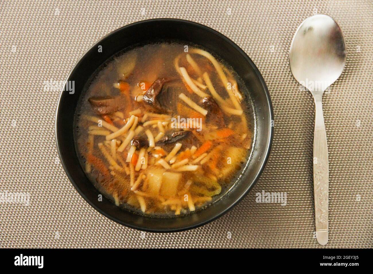 Suppe mit Nudeln und Pilzen in einer schwarzen Keramikschale und Löffel. Blick von oben Stockfoto