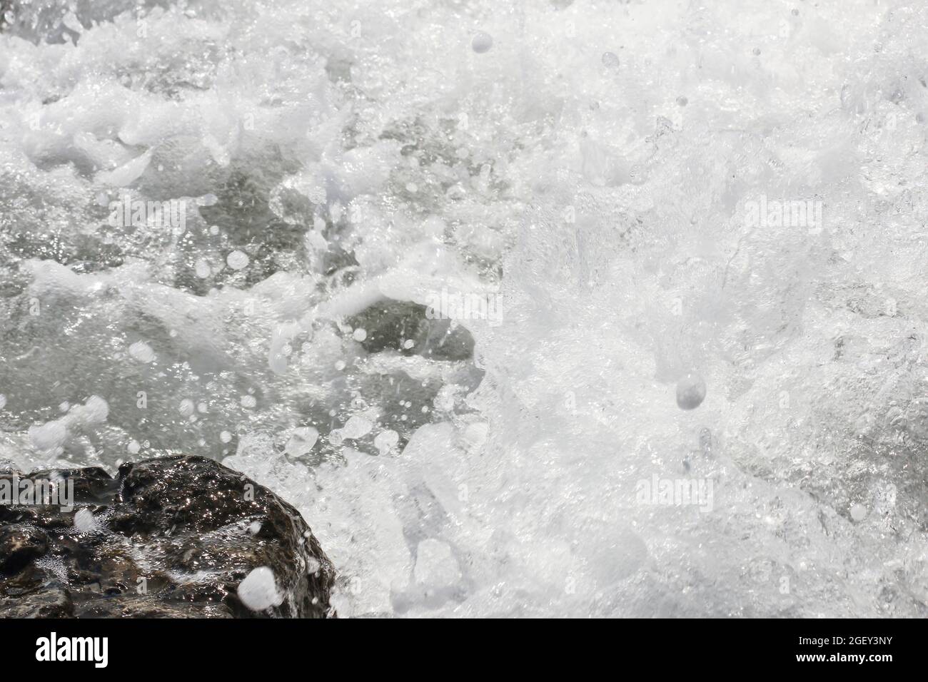 Spritzer von Meereswellen, die gegen Felsen krachen Stockfoto