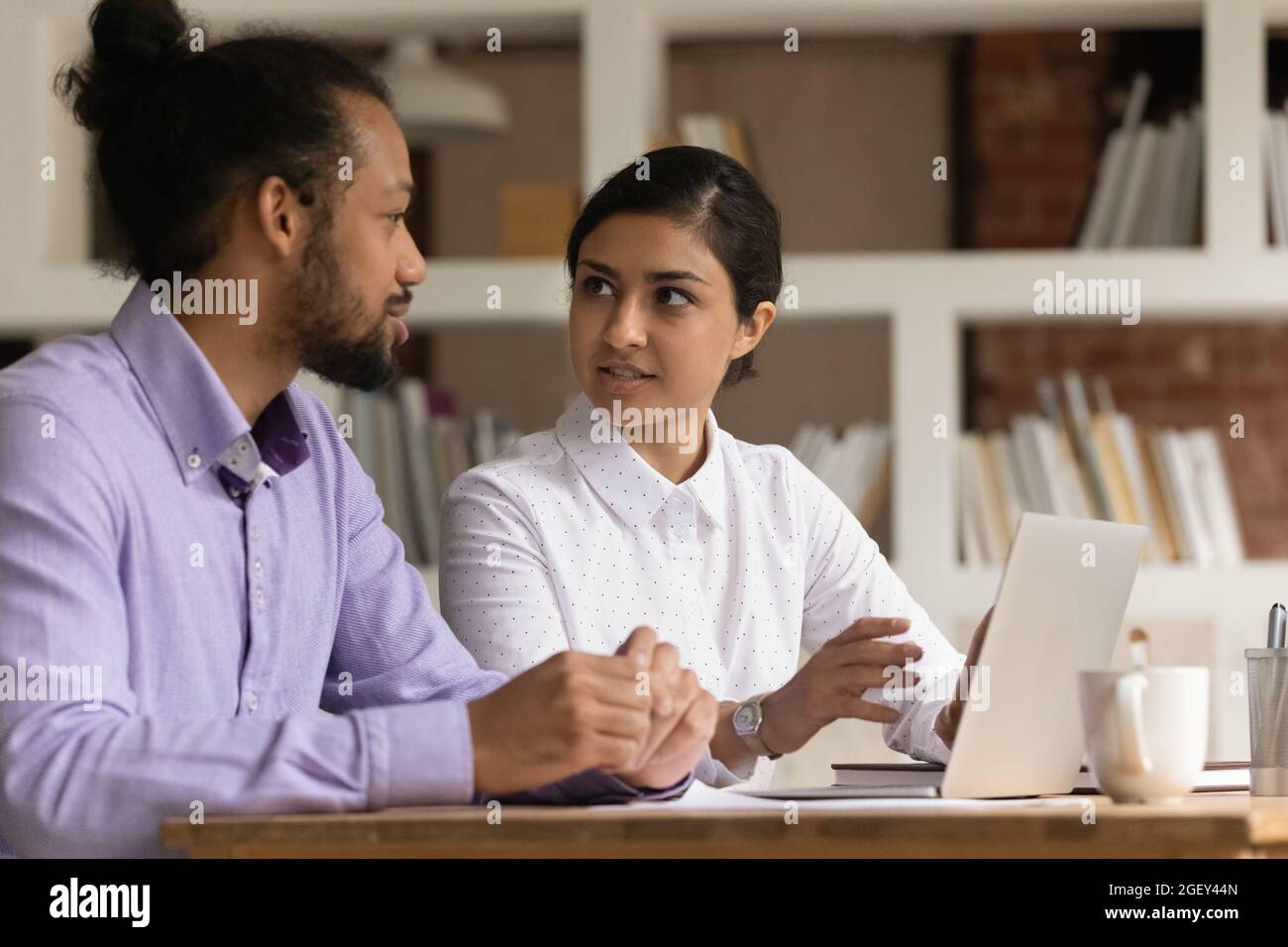 Zwei multiethnische Kollegen sitzen am Schreibtisch und diskutieren über aktuelle Geschäfte Stockfoto