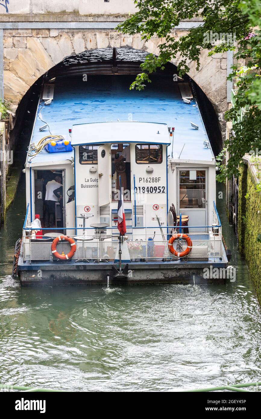 Touristenboot, das unter einer schmalen Brücke des Kanals Saint-Martin in Paris einfährt Stockfoto
