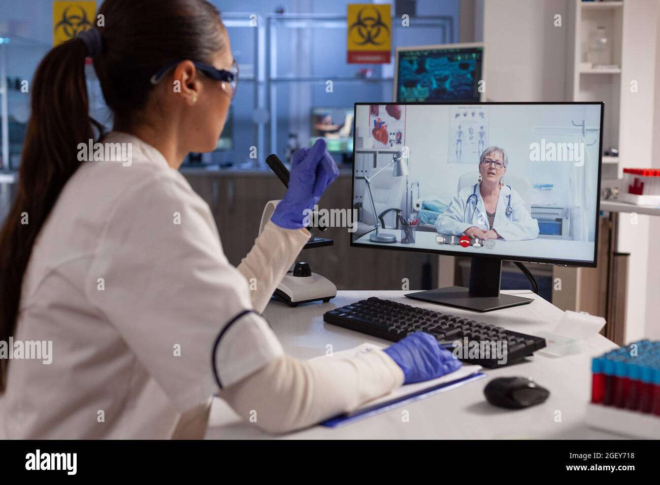 Chemiker, der Videoanruftechnologie auf dem Computer für die Remote-Zusammenarbeit mit dem Spezialisten für Chemieprofessuren verwendet. Forscherin, die sich bei der Untersuchung der Behandlung mit einer Expertin für Viruswissenschaft befasst Stockfoto