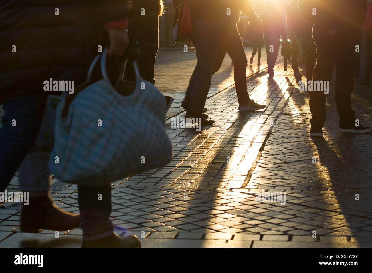 Silhouetten von Pendlern am Morgen mit Sonnenlicht, das während der Hauptverkehrszeit an einem belebten Bahnhof durch die Beine und Füße in Bewegung strahlt Stockfoto