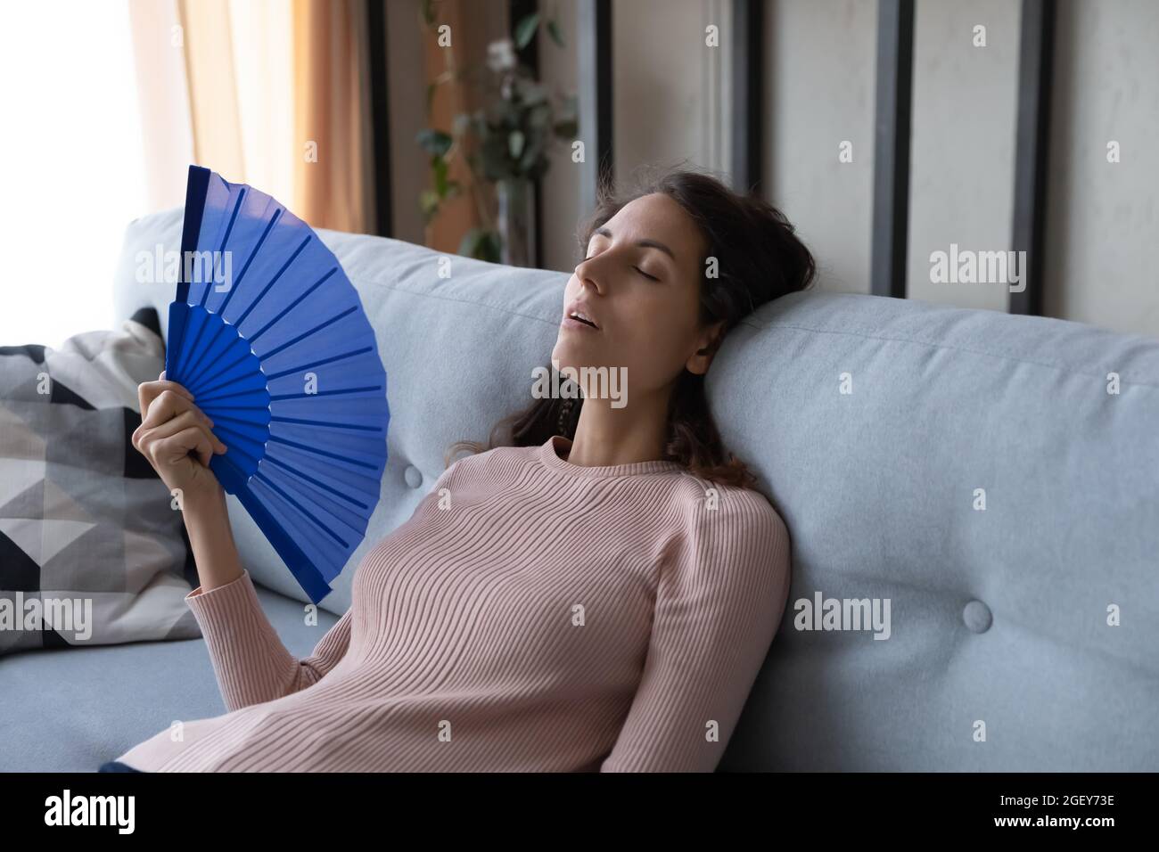 Überhitzte Frau sitzt auf Sofa Wave Handventilator reduzieren Hitze Stockfoto