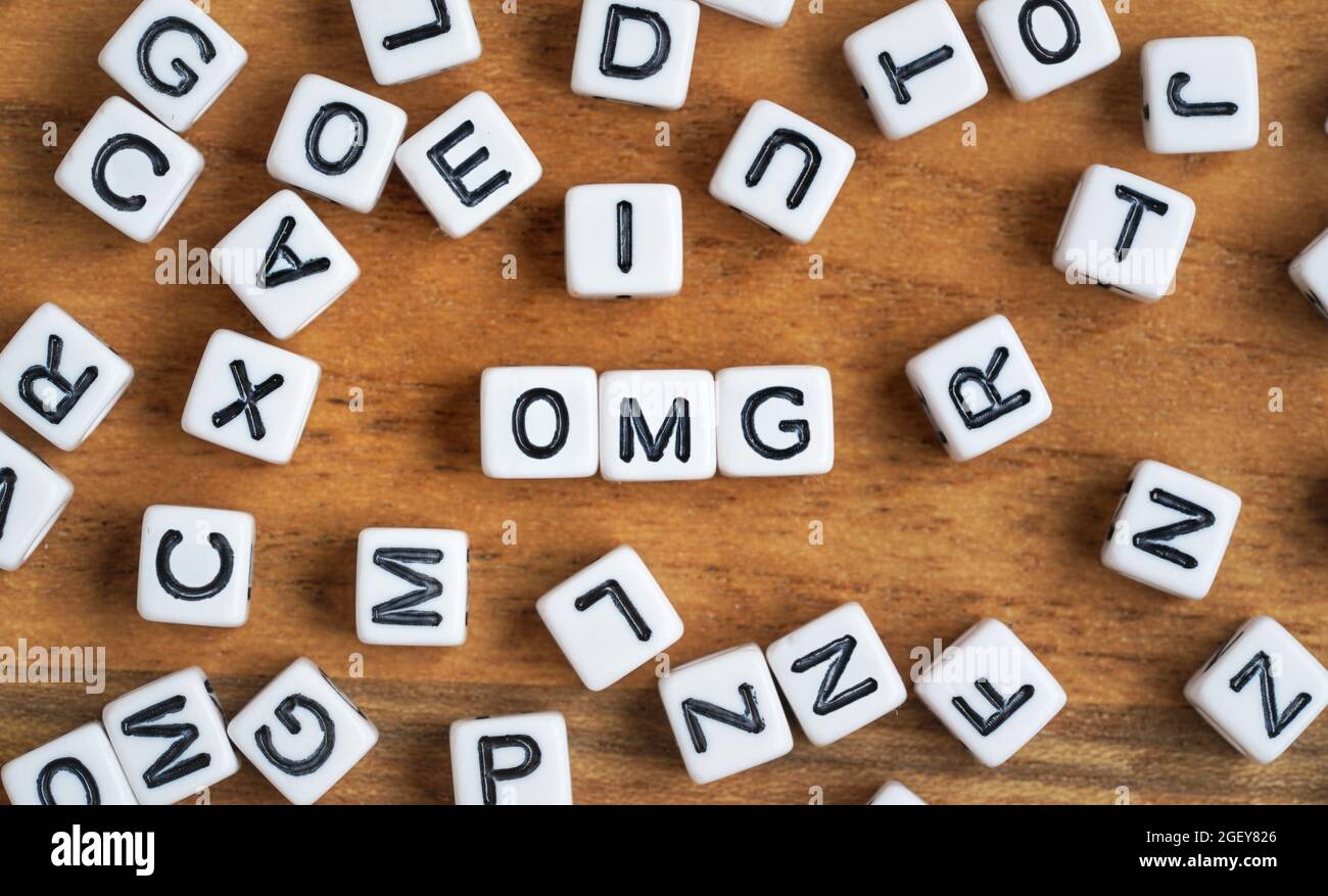 Kleine weiße und schwarze Perlenwürfel auf Holzbrett, Buchstaben in der Mitte buchstabieren OMG. Stockfoto